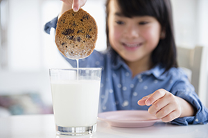 Niña pequeña mojando una galleta en un vaso de leche.